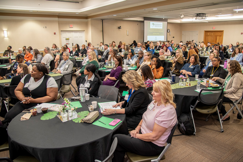 Conference room full of attendees seated at round tables watching stage