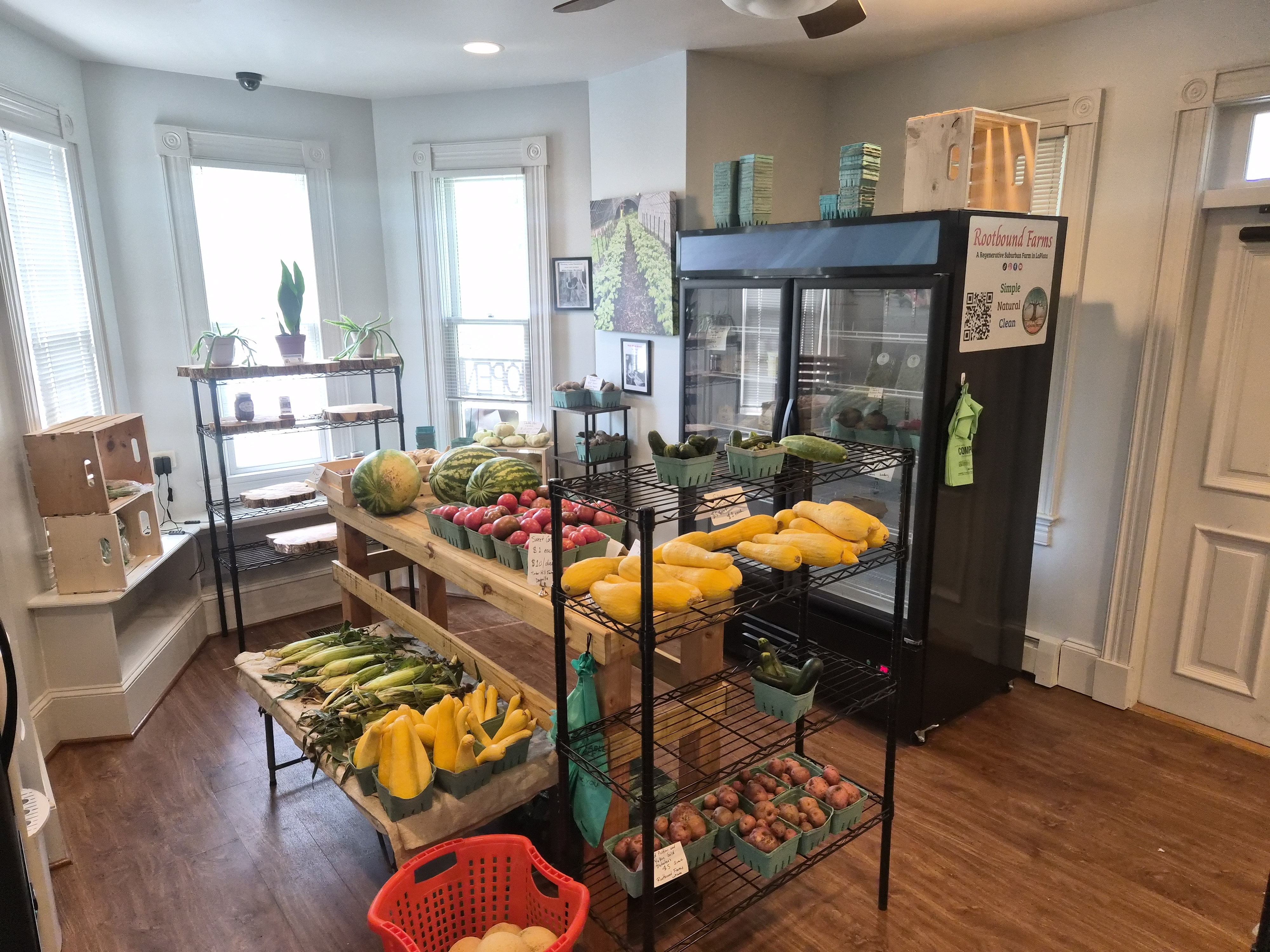 Inside Rootbound Farms with a store rack filled with fresh produce, large stand up cooler, and rack with jams. 