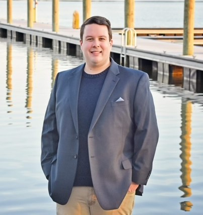 CSM graduate Brandon Russell, wearing a suit jacket and smiling at the camera in front of a body of water