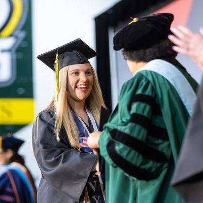 CSM graduate Loren Eiland, dressed in graduation cap and gown, smiles and shakes hands with CSM President Yolanda Wilson