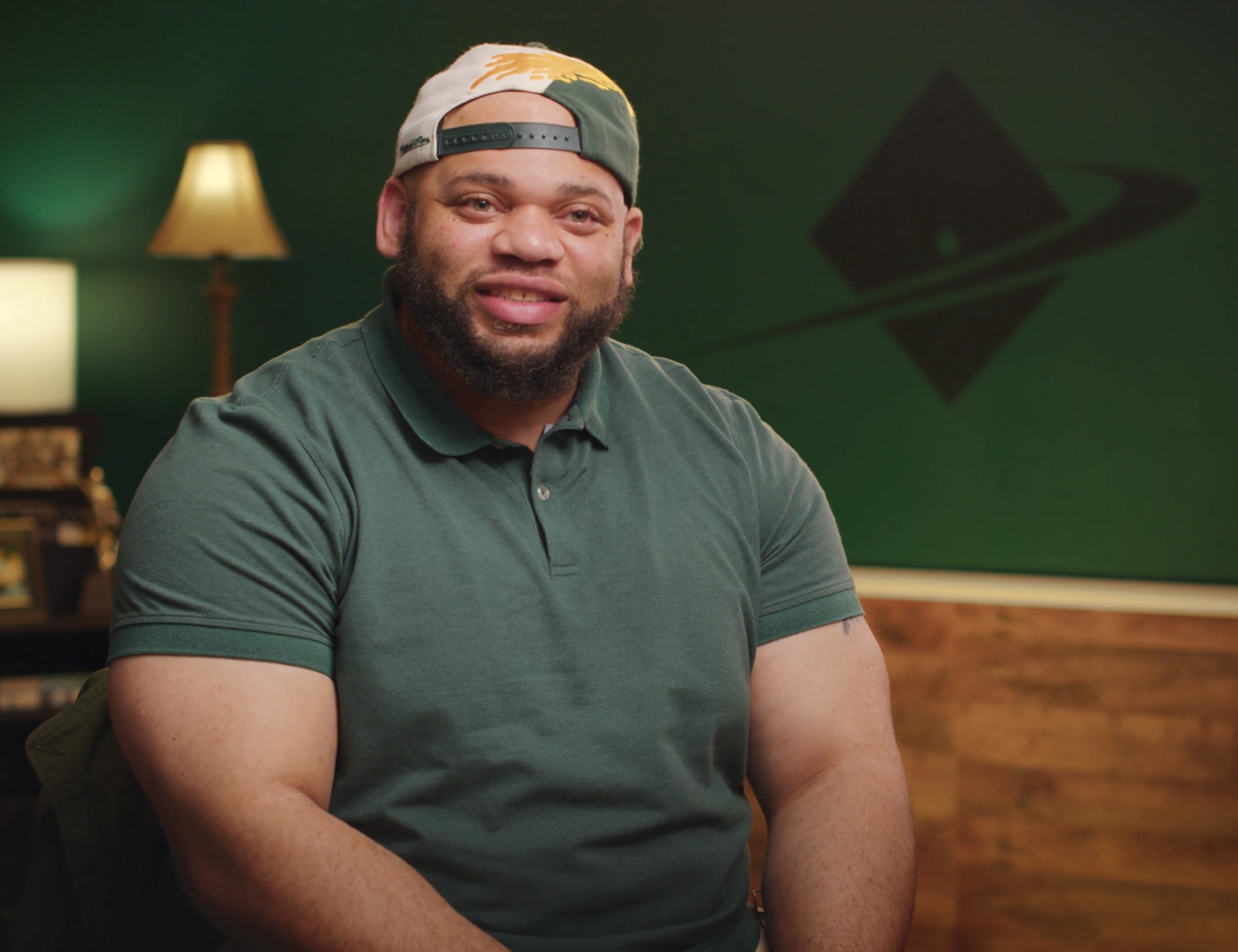 CSM graduate John Jones, smiling and talking to someone out of the frame, sitting in a cozy interview space.