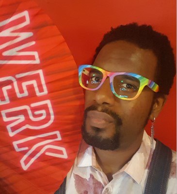 A selfie of CSM alum Kenny Waters, wearing glasses with rainbow colored frames and holding a fan reading "WERK"