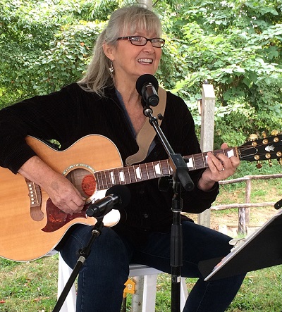 Former CSM student Lois Stephenson, a woman with light hair, playing an acoustic guitar and singing into a microphone