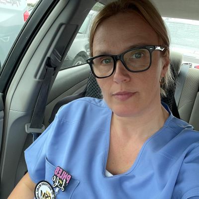 Selfie of CSM alumna Monika Boscato, a blonde woman wearing glasses and light blue hospital scrubs