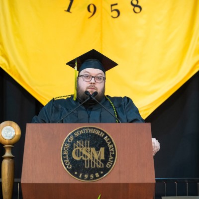 Photo of CSM graduate Robbie Katzberg in graduation regalia standing at a podium