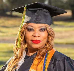 woman standing outside smiling in cap and gown