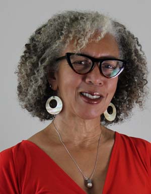 Woman with dark curls in black cat-eye glasses, large earrings, and a red shirt