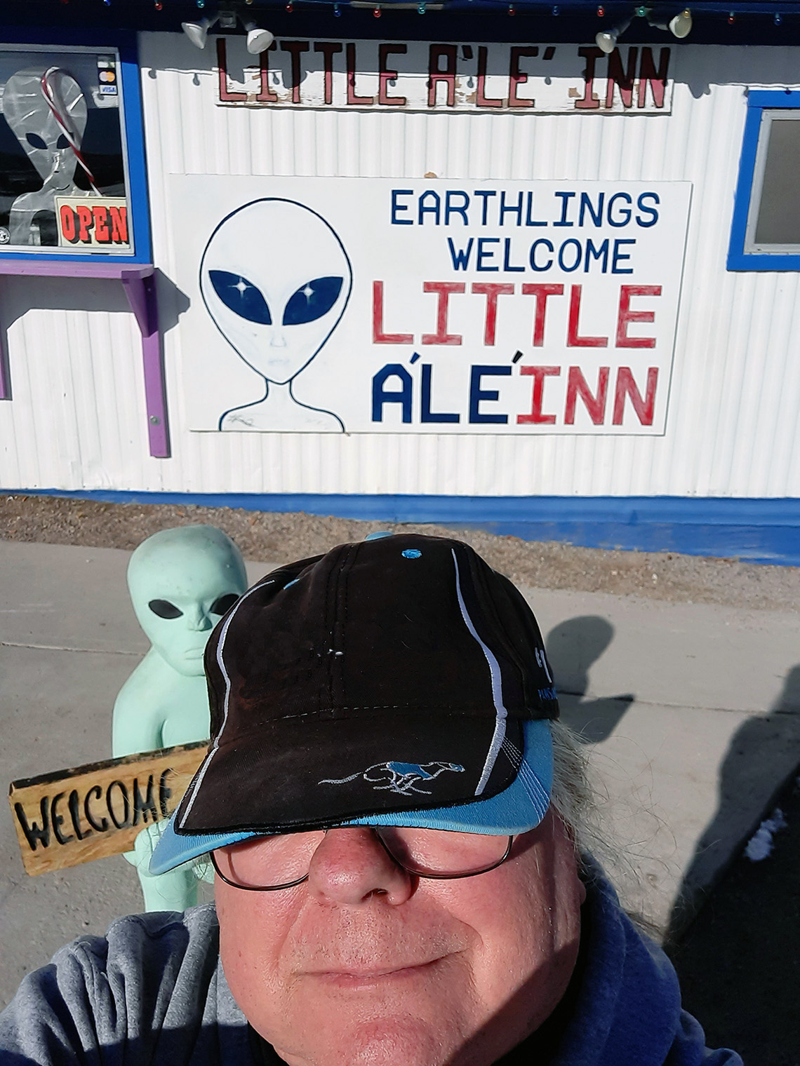 A selfie of CSM art instructor Gary Jameson, wearing a black and blue baseball cap, standing in front of an extraterrestrial-themed inn