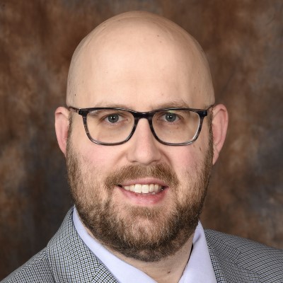 Professional headshot of History Professor Dr. John Mohr, a smiling man with glasses and a beard and wearing a suit