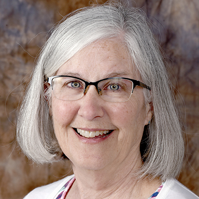 A professional headshot of CSM bio science professor Lori Crocker. She is smiling at the camera and is wearing a white button-up top over a floral print top.