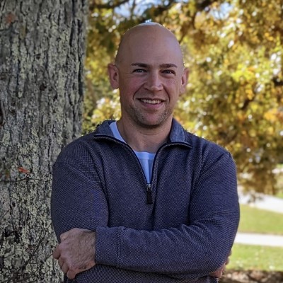 A photo of CSM instructor standing outdoors beside a tree with golden leaves