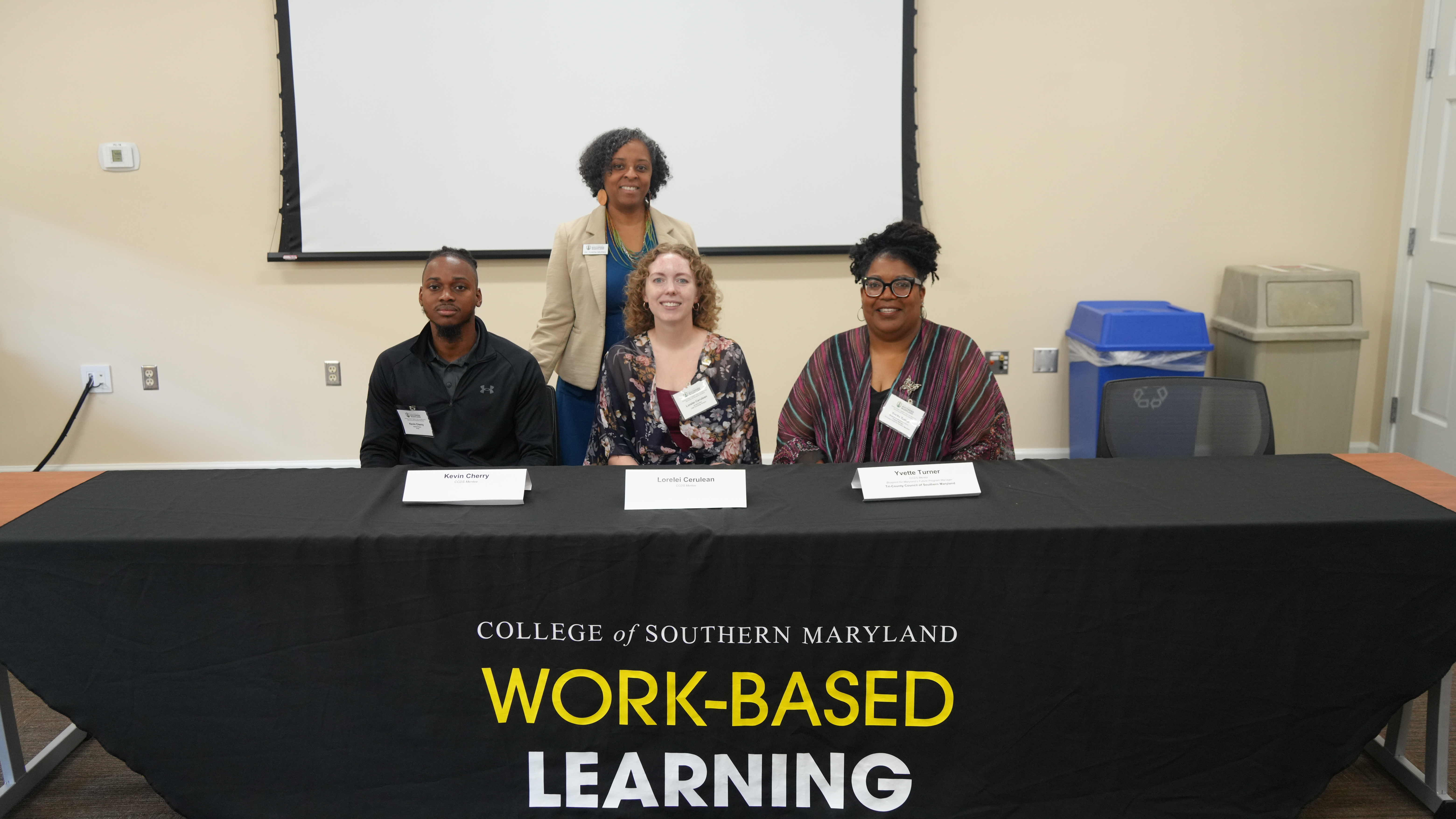 Mentors and mentees sit at table with black table cloth which reads 'work based learning'