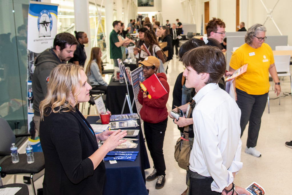 Event attendees stand at a row of information tables 