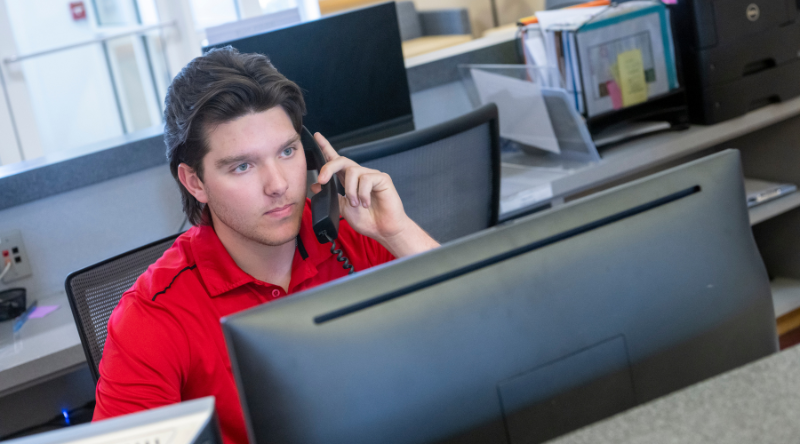 person at a desk on the phone looking at a computer