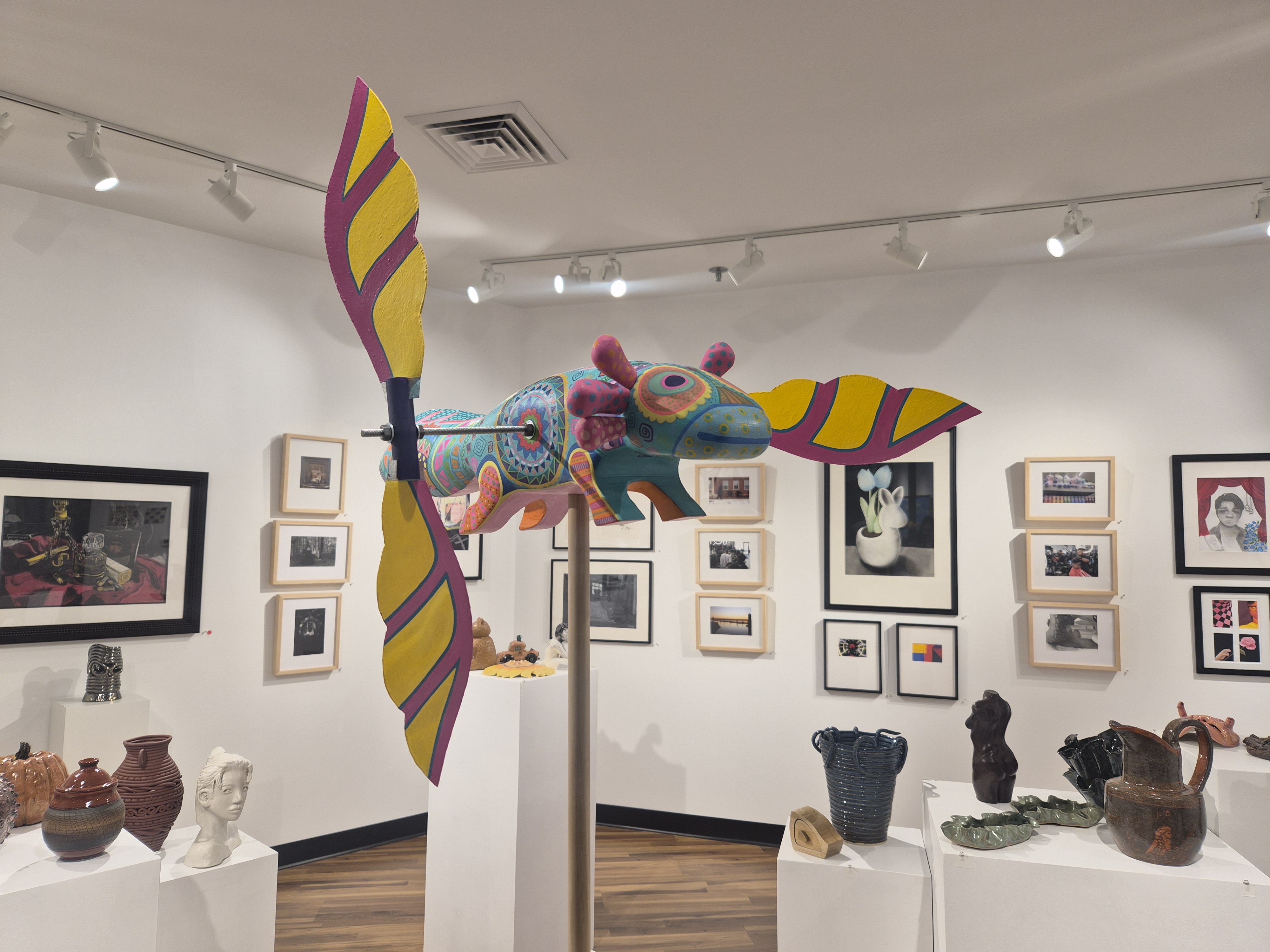 Art gallery filled with clay pots, a brightly animal sculpture, and paintings on the wall