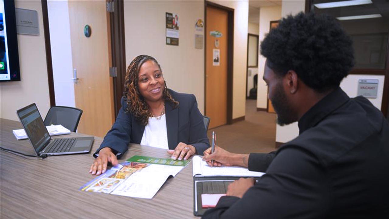 A woman in business attire smiles while discussing documents with a man during a meeting at an office.