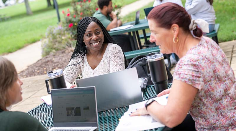 Students work on their laptops while sitting at an outside table