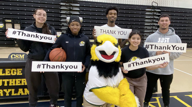 Student athletes pose with the Hawk mascot holding signs saying thank you