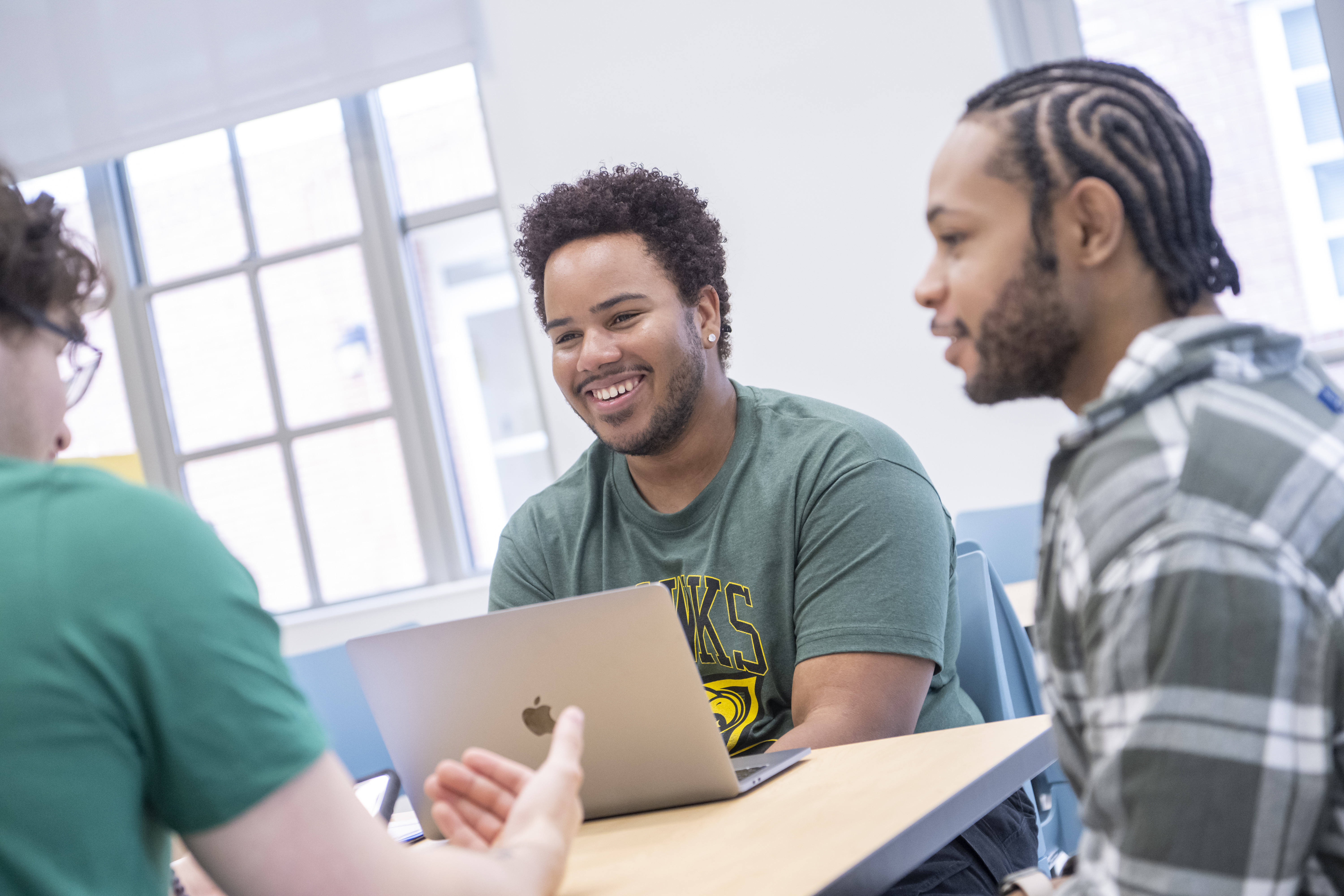 Three young adults sit around a table smiling with one on a laptop