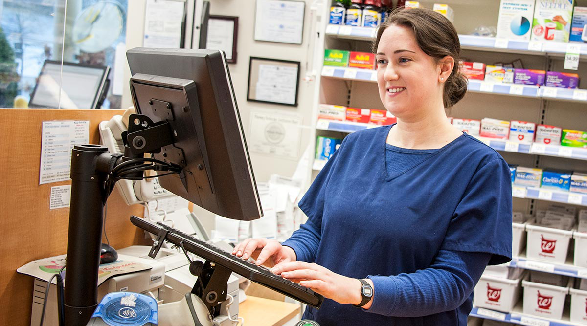Pharmacy Technician typing at computer and smiling