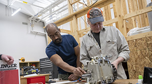 two men using a hand held machine on a work bench