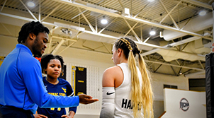 man on basketball court talking to two women playing the sport
