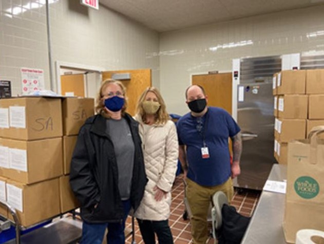 Group of three people stand in a room filled with boxes of food